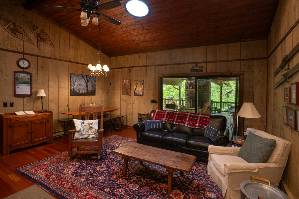 A bright, inviting living area with a leather sofa, wooden coffee table, and a dining table set near a large window. The open layout is ideal for entertaining, playing games, or enjoying a meal together, while natural light streams in, framing views of the outdoors.