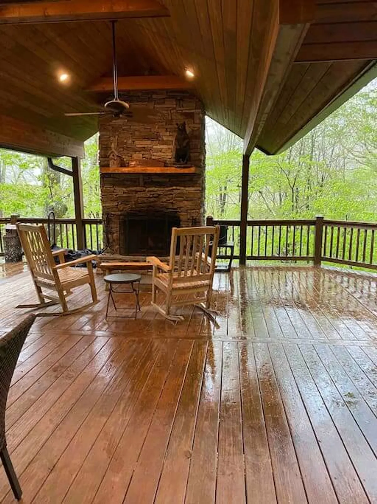 A cozy exterior deck featuring wooden rocking chairs, a stone fireplace, and scenic forest views. The space looks inviting for relaxing après-ski, sipping a warm drink, or gathering with friends, especially after a day on the mountain.