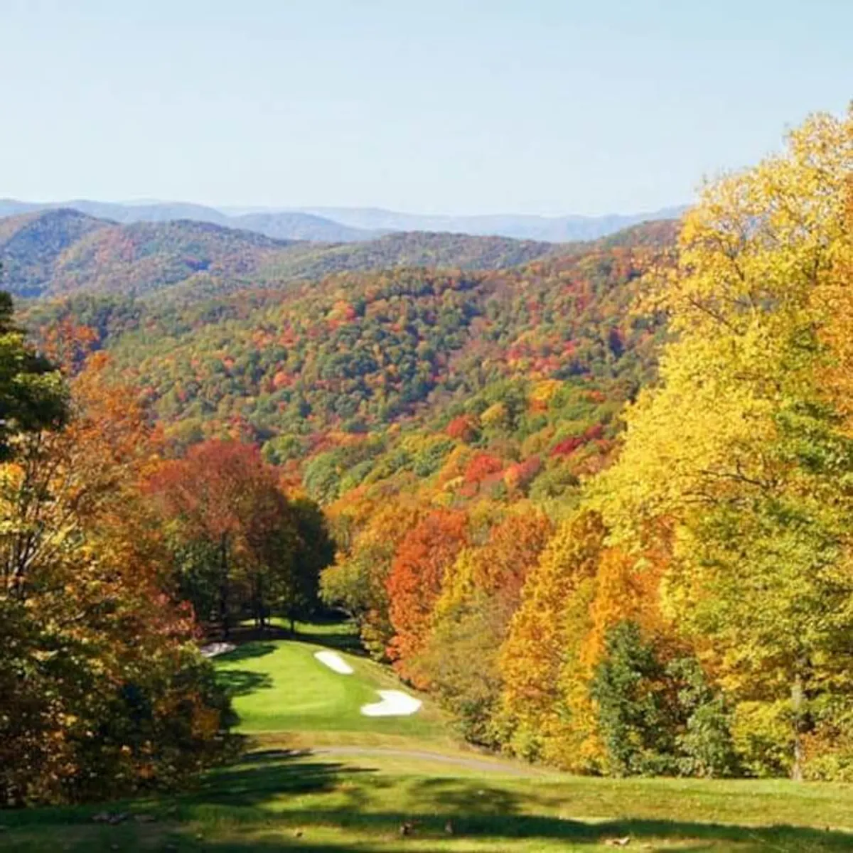 A sweeping view of a lush golf course framed by vibrant autumn foliage, with majestic mountains rising in the background. The scene is serene and expansive, capturing the natural beauty and tranquility of the resort's setting.