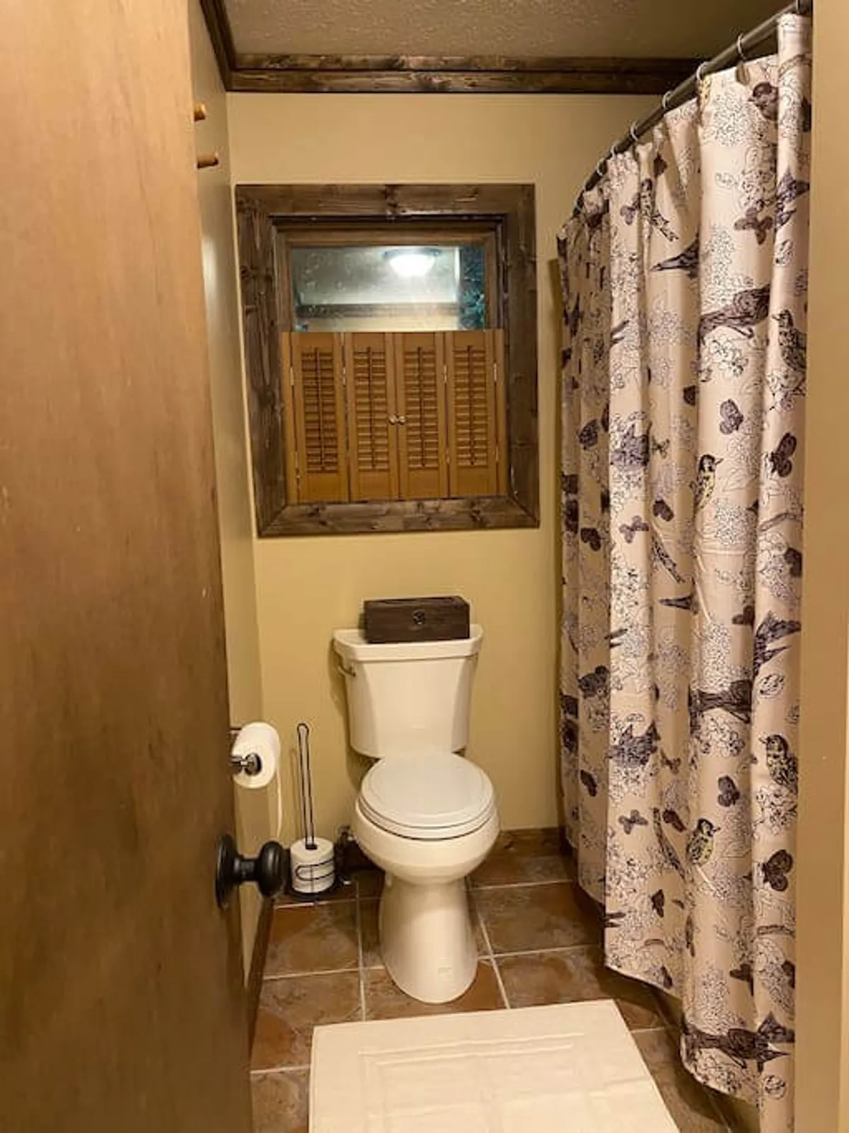 A bathroom interior with a toilet, shower curtain, window with wooden framing, and comfortable flooring, creating a clean and peaceful atmosphere suitable for self-care and refreshment.