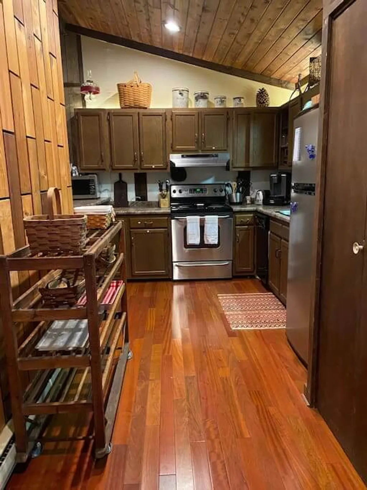 A welcoming kitchen featuring a stainless steel stove, warm wooden cabinets, open shelving with woven baskets, and glowing wooden flooring. The countertops provide ample prep space, and the kitchen radiates a cozy, social atmosphere ideal for both casual family meals and special occasions.
