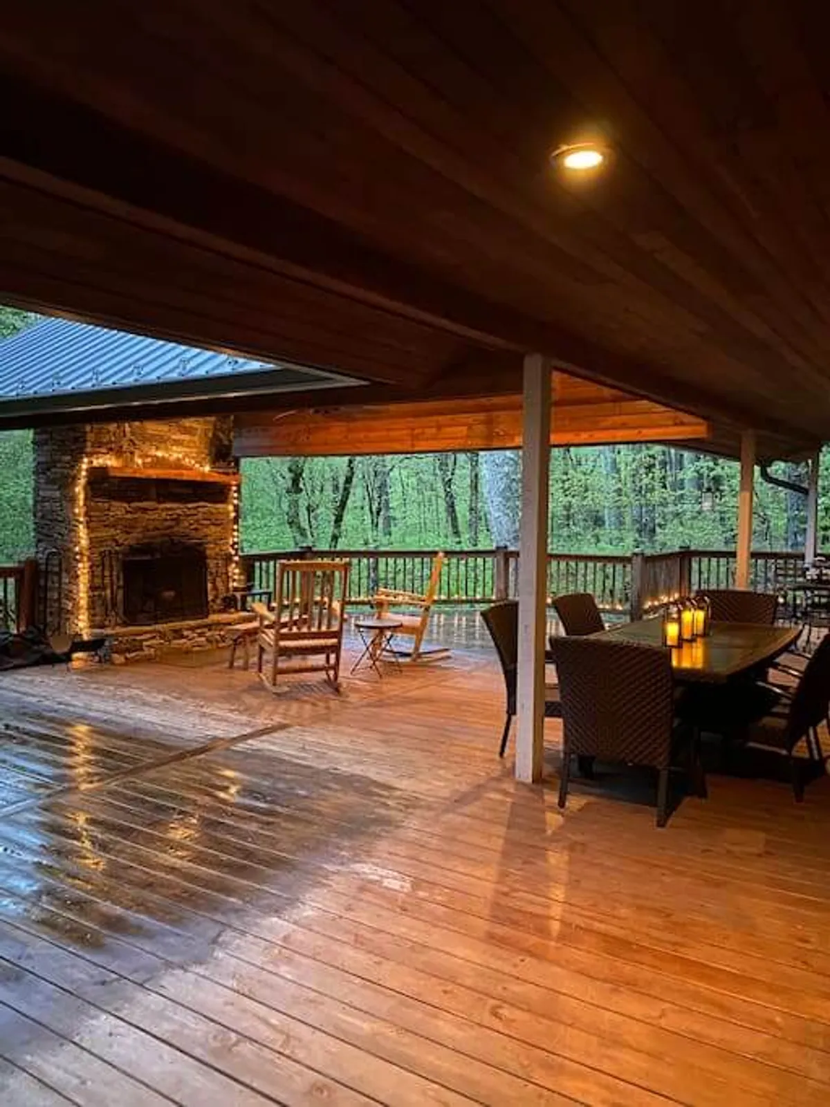 An inviting outdoor scene with a stone fireplace as its centerpiece, surrounded by a dining table set for a meal, rocking chairs, and softly glowing candles. The ambiance is warm and welcoming, encouraging guests to gather, dine, and share stories as night falls or during cool mountain evenings.
