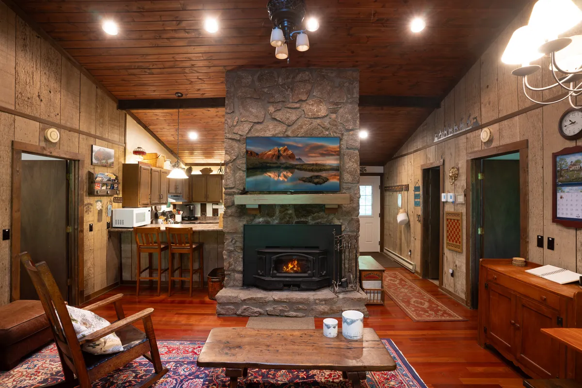 A cozy living room scene centered around a robust stone fireplace, with plush seating and a wooden table. Artwork above the fireplace adds warmth and personality, while the furnishings are arranged for conversation and comfort. The overall mood is intimate and welcoming—ideal for relaxing after outdoor adventures.